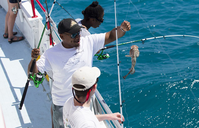 A student catches a fish while fishing on a fishing boat.