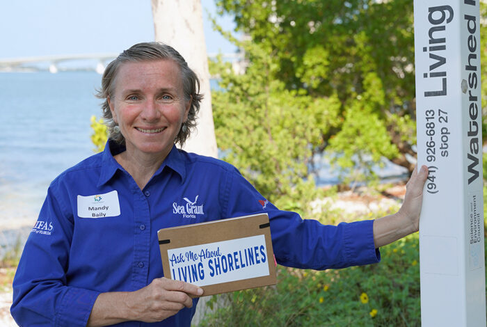 mandy baily standing next to a living shoreline in Sarasota with a "Ask Me About Living Shorelines" sign