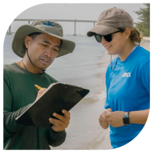 man and woman at waterline monitoring shorelines with bridge in background