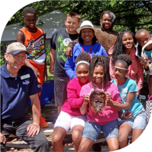 group of kids outside holding a horseshoe crab skeleton posing for photo with teacher and with trees in background