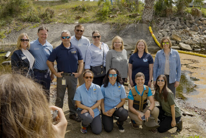 operation trap leaders pose for photo in front of litter collection device in creek