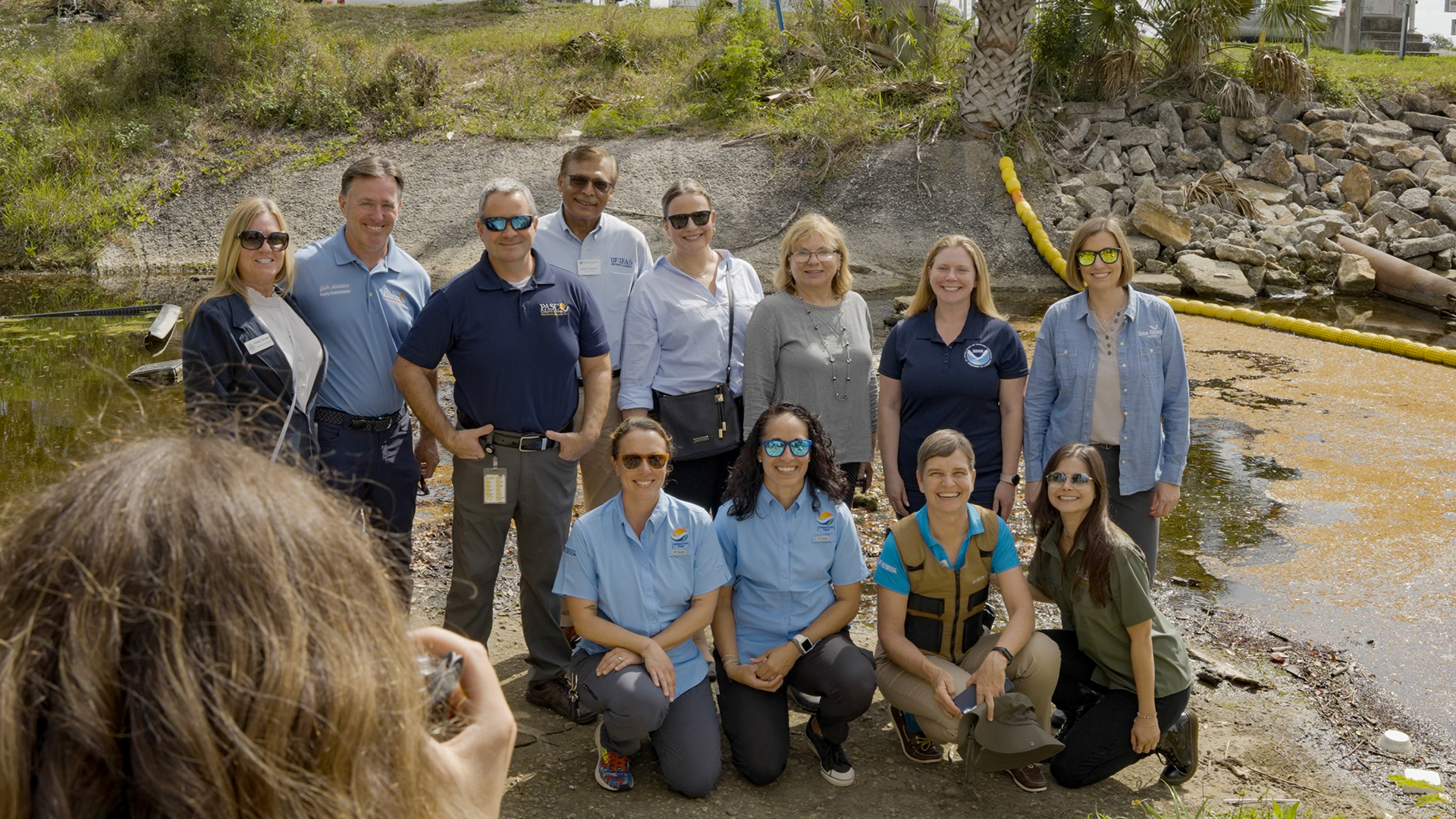 operation trap leaders pose for photo in front of litter collection device in creek