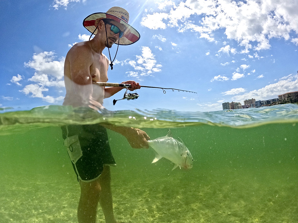 man standing in ocean holding rod in one hand and fish tail in another