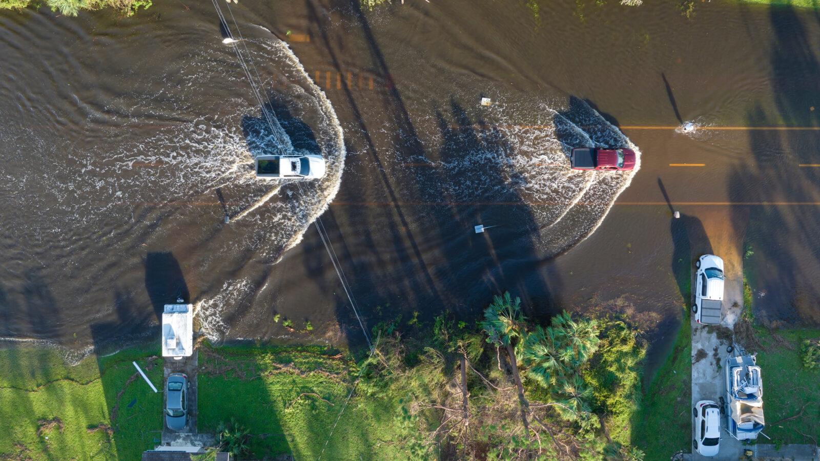 Flooded Florida road with evacuating cars and surrounded with water houses in suburban residential area. Consequences of hurricane natural disaster