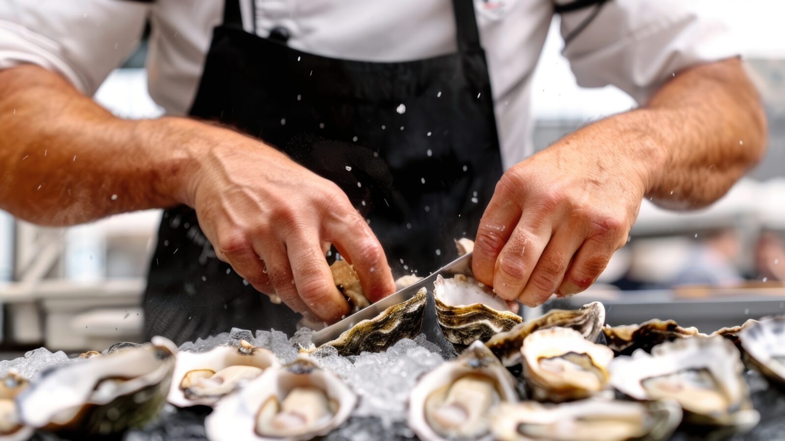 A close-up of a chef shucking fresh oysters with a knife over a bed of crushed ice.