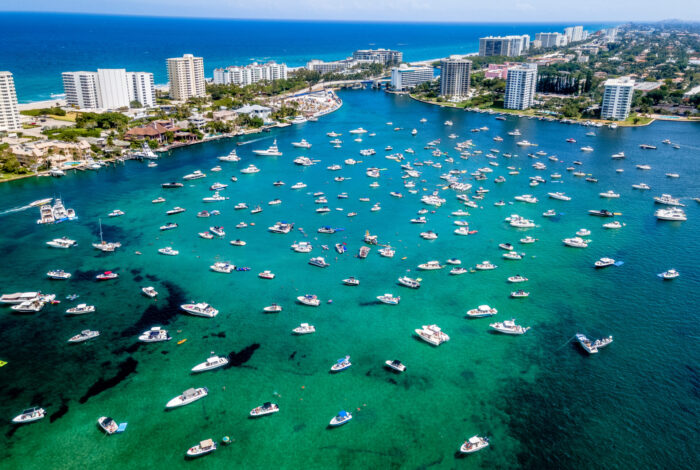 aerial shot of boats on a bright turquoise waterway surrounded by coastal high-rise buildings and the ocean in the background.