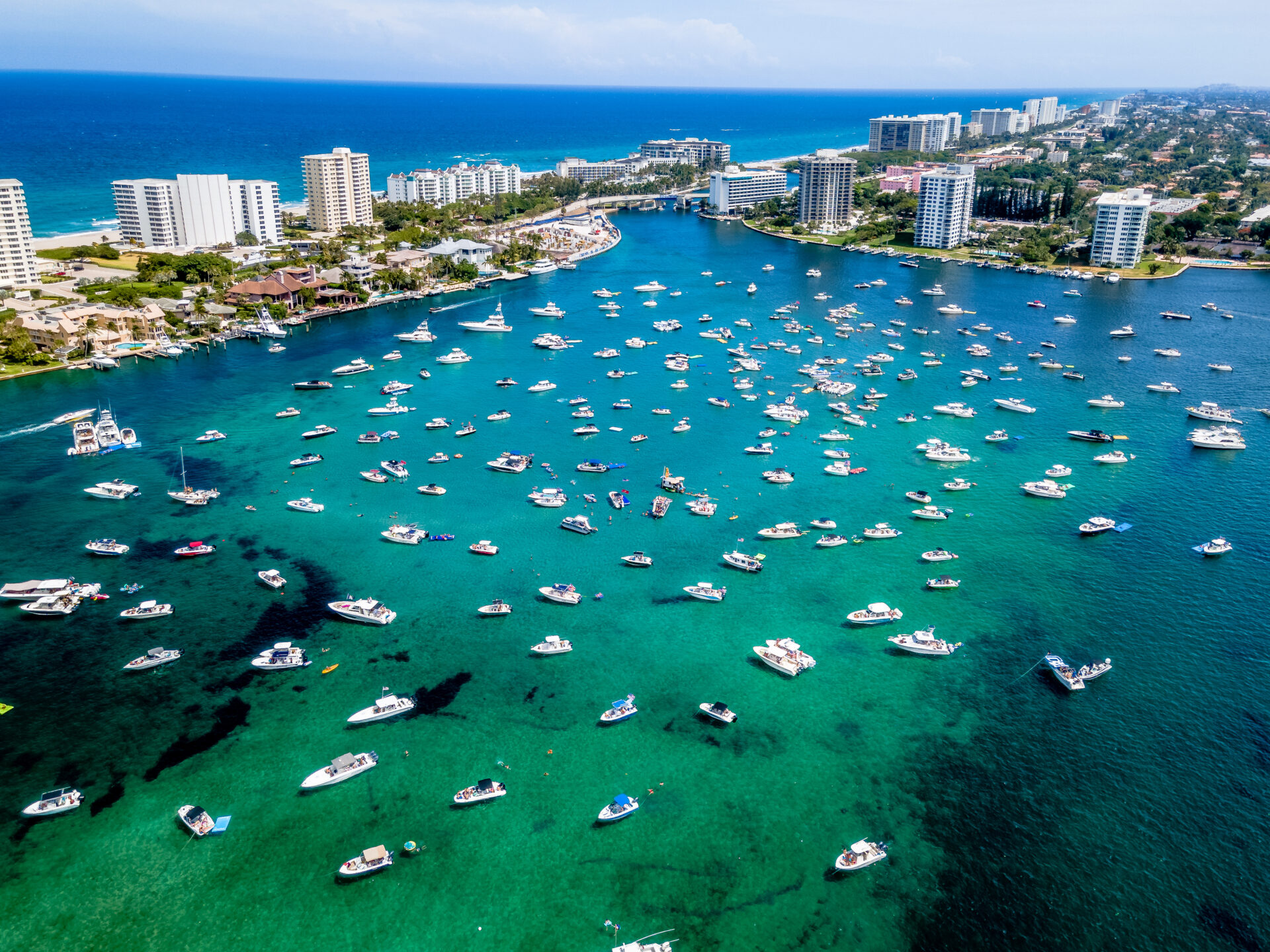 aerial shot of boats on a bright turquoise waterway surrounded by coastal high-rise buildings and the ocean in the background.