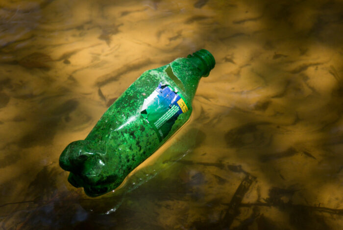 a green plastic bottle floating in shallow water