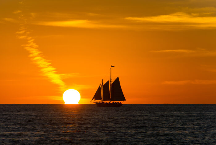 sailboat in ocean with with the sun touching the water in the background