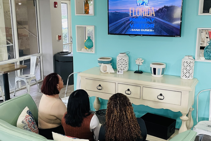 three people sitting on a couch watching a television with florida friendly visitor on the screen