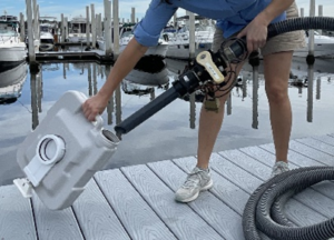 person on a dock holding a portable toilet waste tank and inserting into it a suction wand attached to a pumpout hose