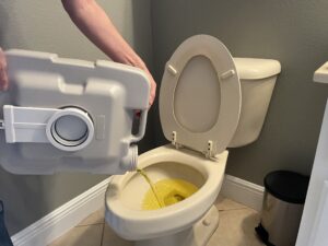 hands holding a portable toilet waste tank being poured into a landside toilet