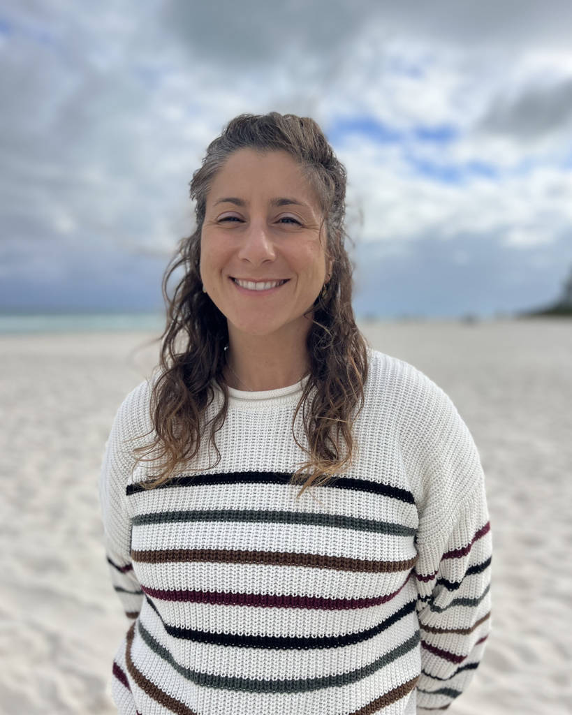 Gina Clementi smiling in front of sandy shoreline.