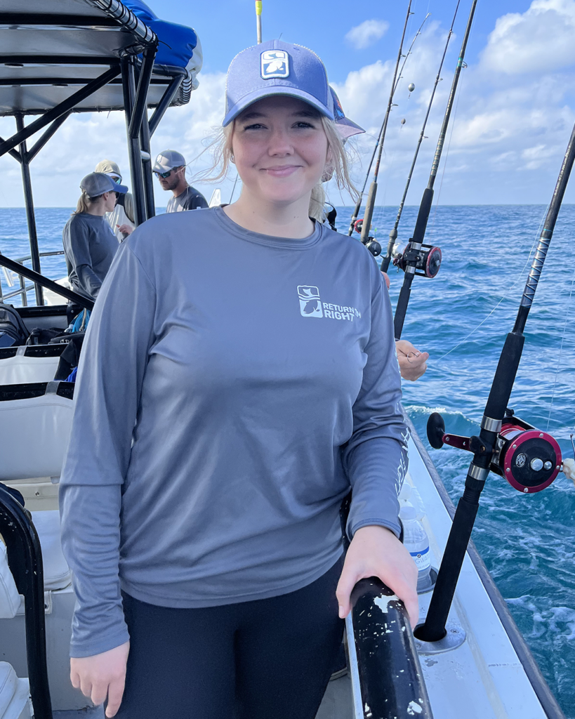 Selia Zimmerman poses on a fishing boat with fishing rods beside her.