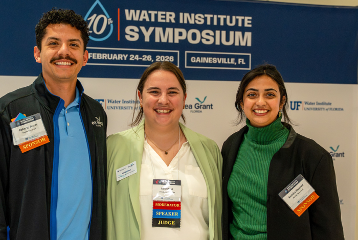 Roberto Ferrer, Kate Rose and Sarisha Boodoo posing in front of a water institute symposium banner