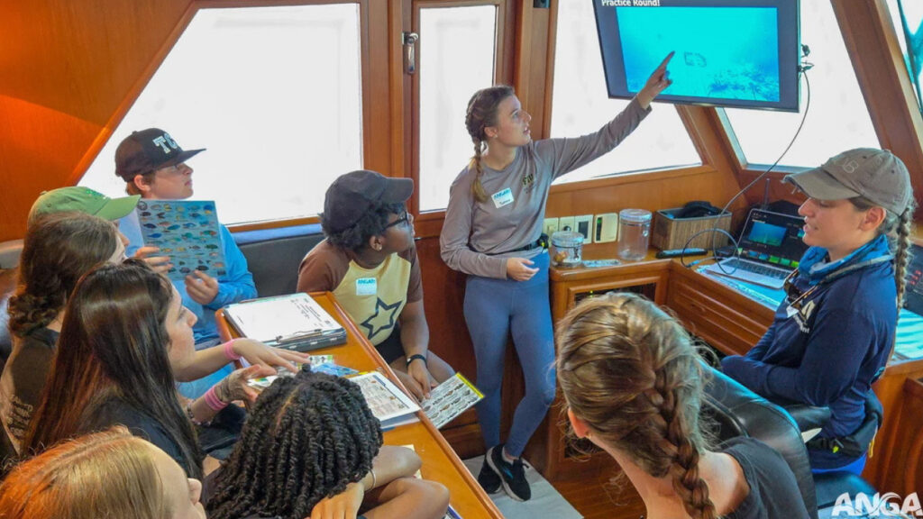 Sophia points at a screen while demonstrating her research as a group of young onlookers observes.