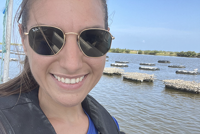 Dr. Sharon Cilano smiling in front of floating oyster cages above water.