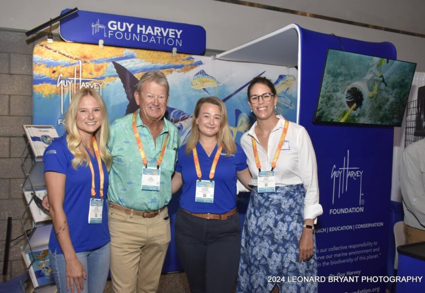Two 2024 FSG-Guy Harvey Fellow posing with Dr. Guy Harvey and his daughter, Jessica Harvey, in front of banner.