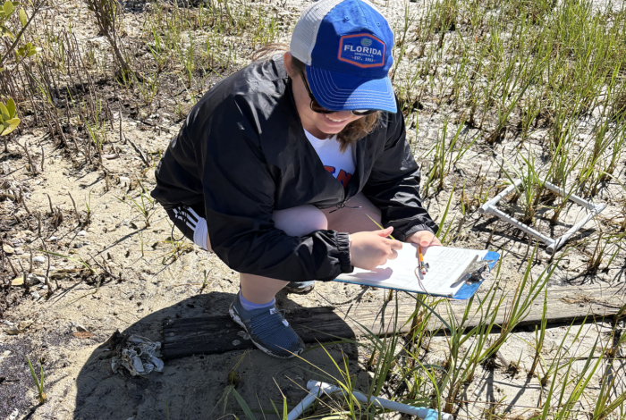 Undergraduate intern with clipboard and quadrat, collecting coastal vegetation data.